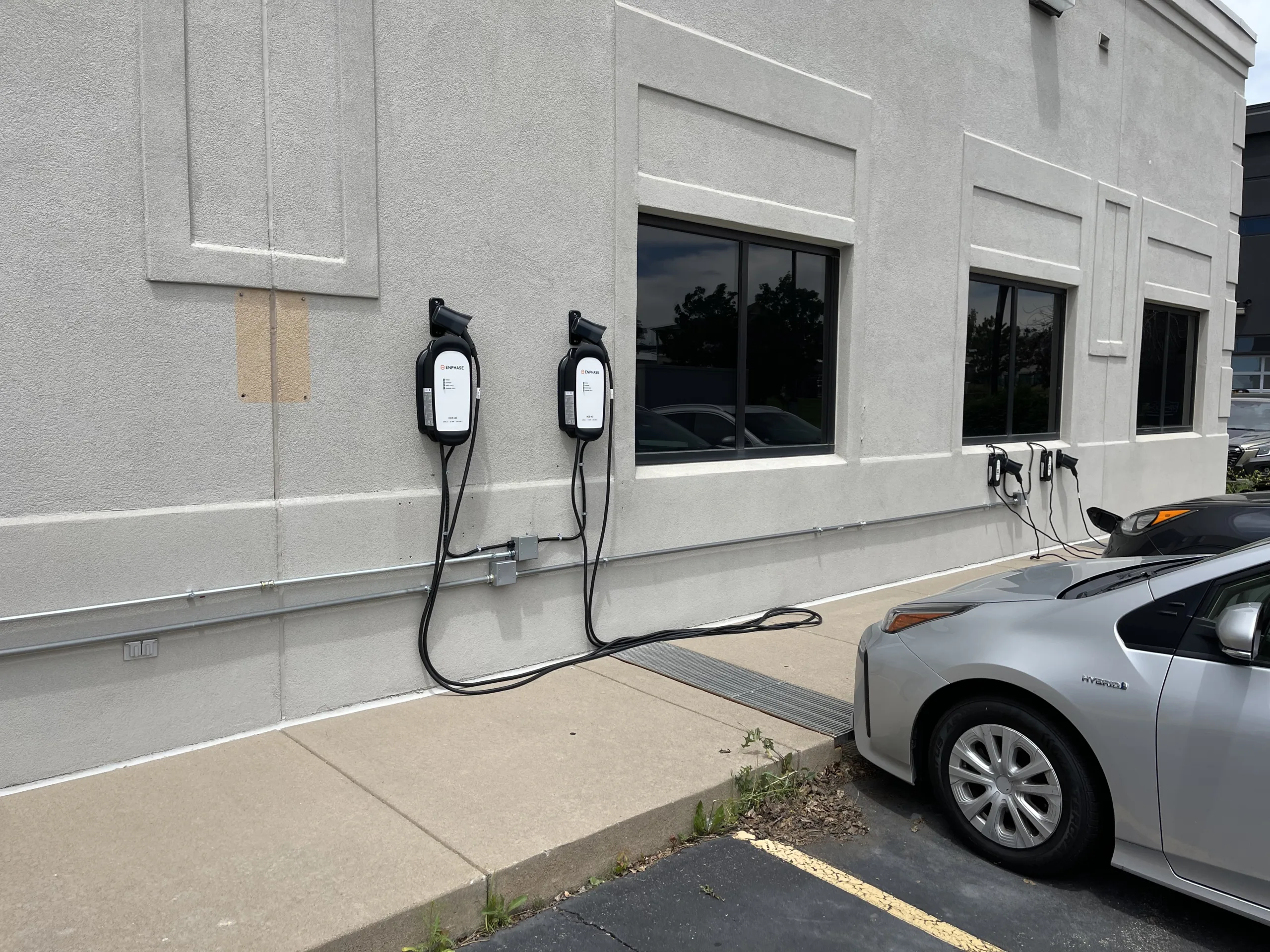 A depiction of two cars parked by an electric charging station in front of a building, illustrating our electrician contractor services for installation and repairs
